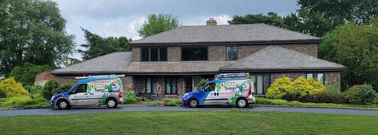 Two vans in a driveway in front of a home with green grass in front.