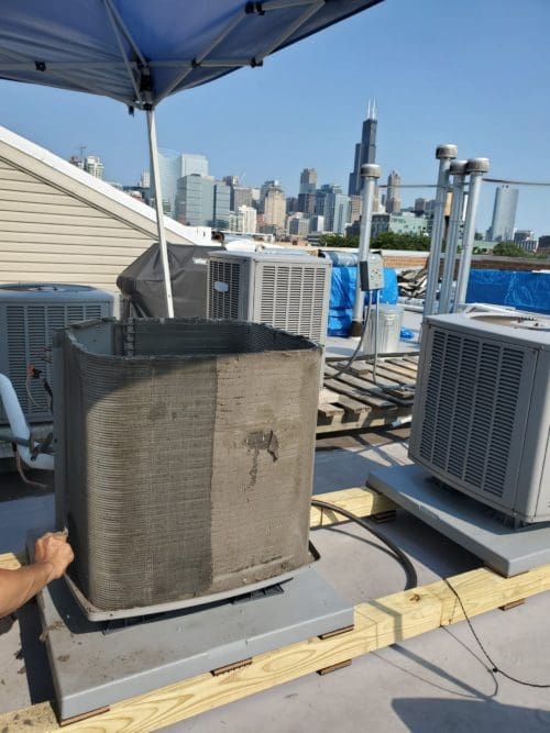 An extremely dirty air conditioner on a Chicago rooftop needs an AC tune up.