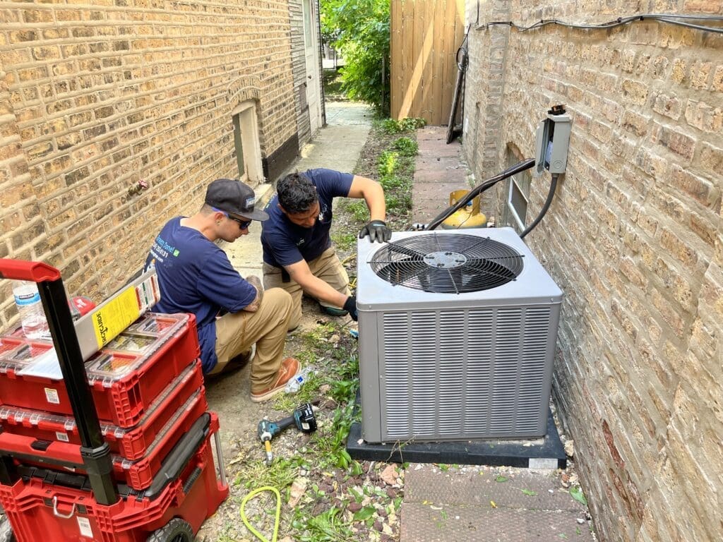 Two HVAC technicians working on an air conditioner.