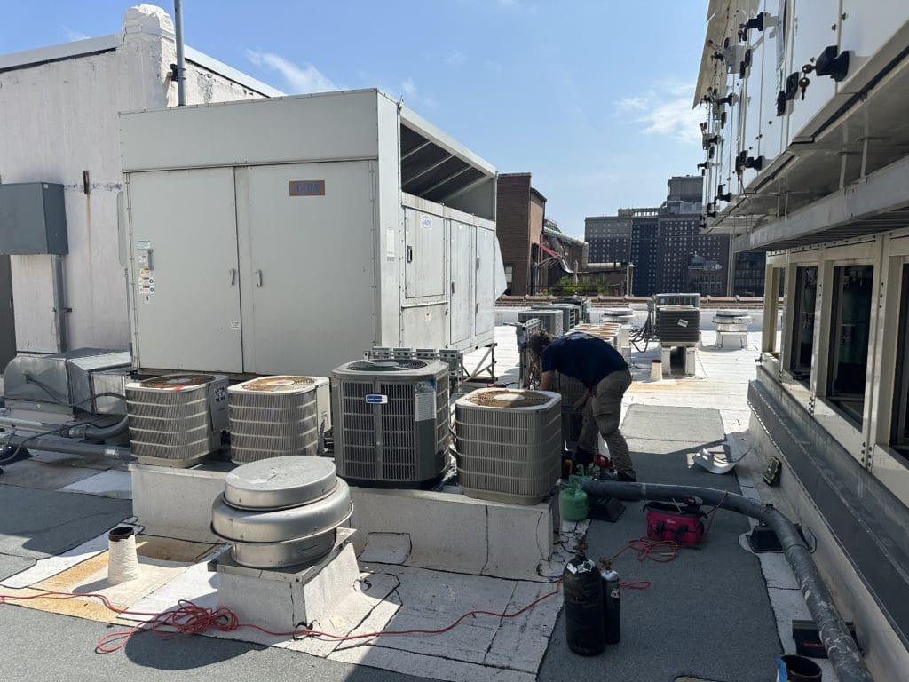 An HVAC technician on a rooftop installing new air conditioners.