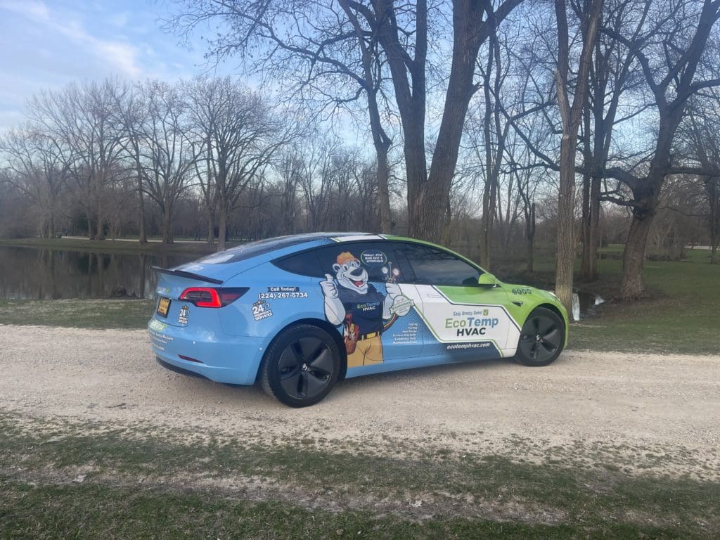A Tesla Model 3 wrapped in Eco Temp HVAC logos on a dirt road in Wilmette IL.