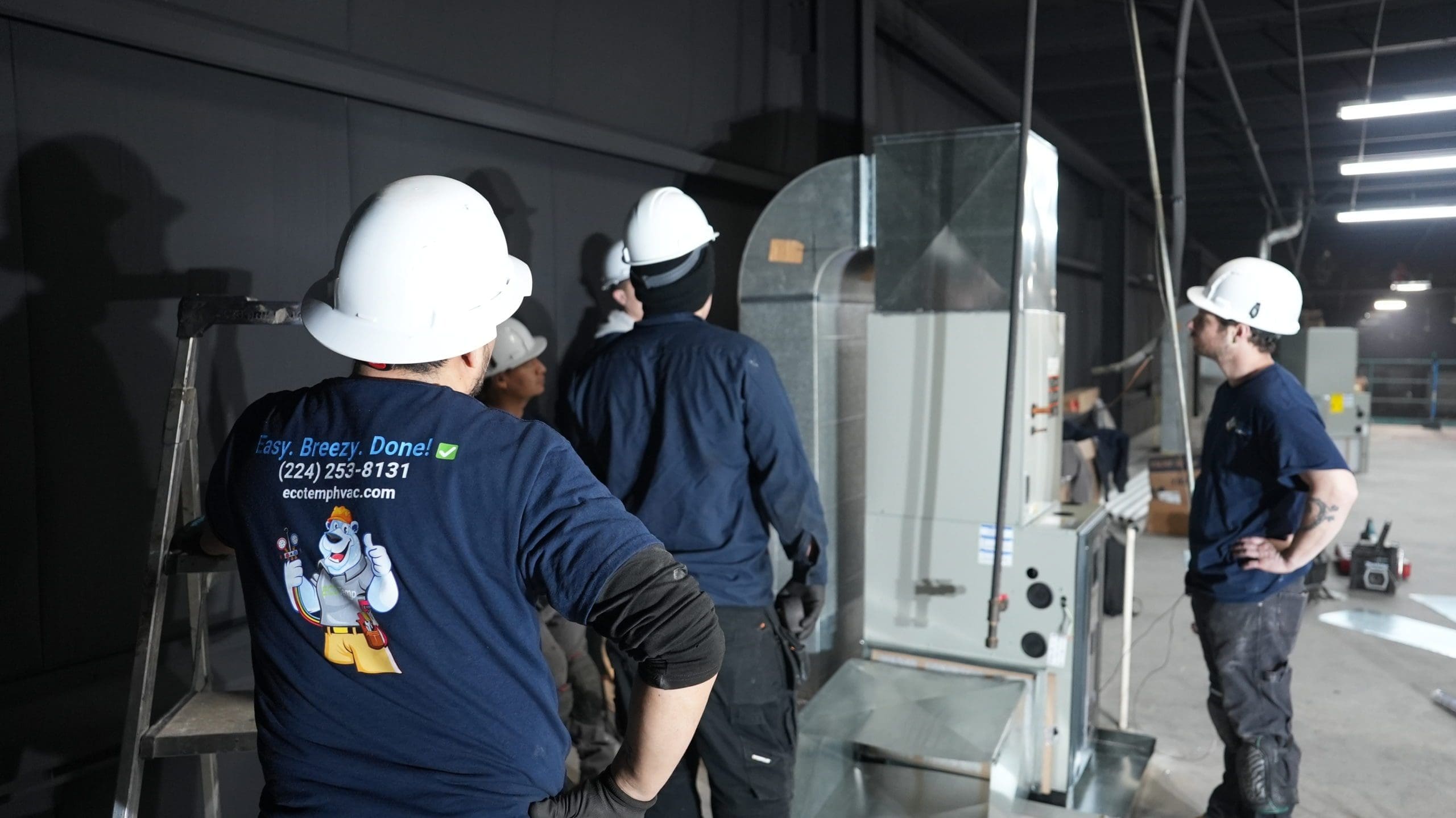 Five HVAC technicians standing near a furnace.