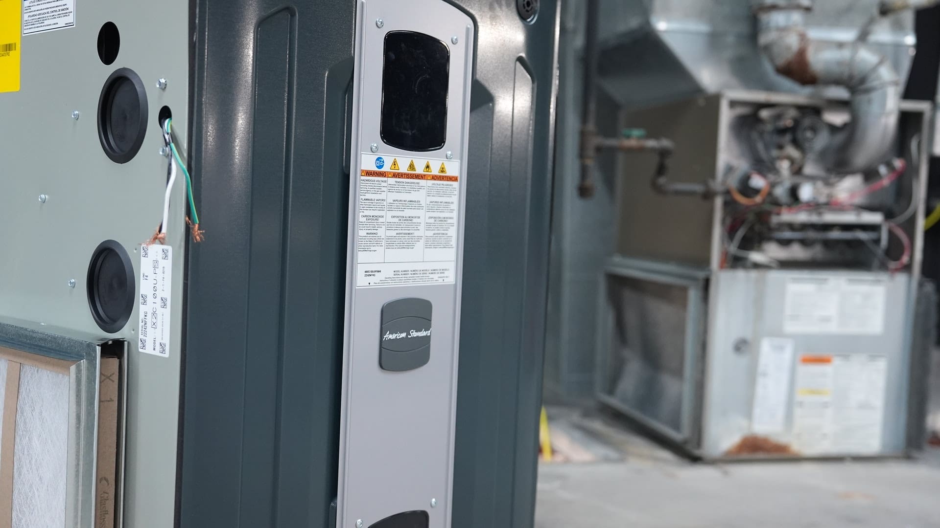 A photo of a furnace with an American Standard logo on it with an uncased furnace in the back.